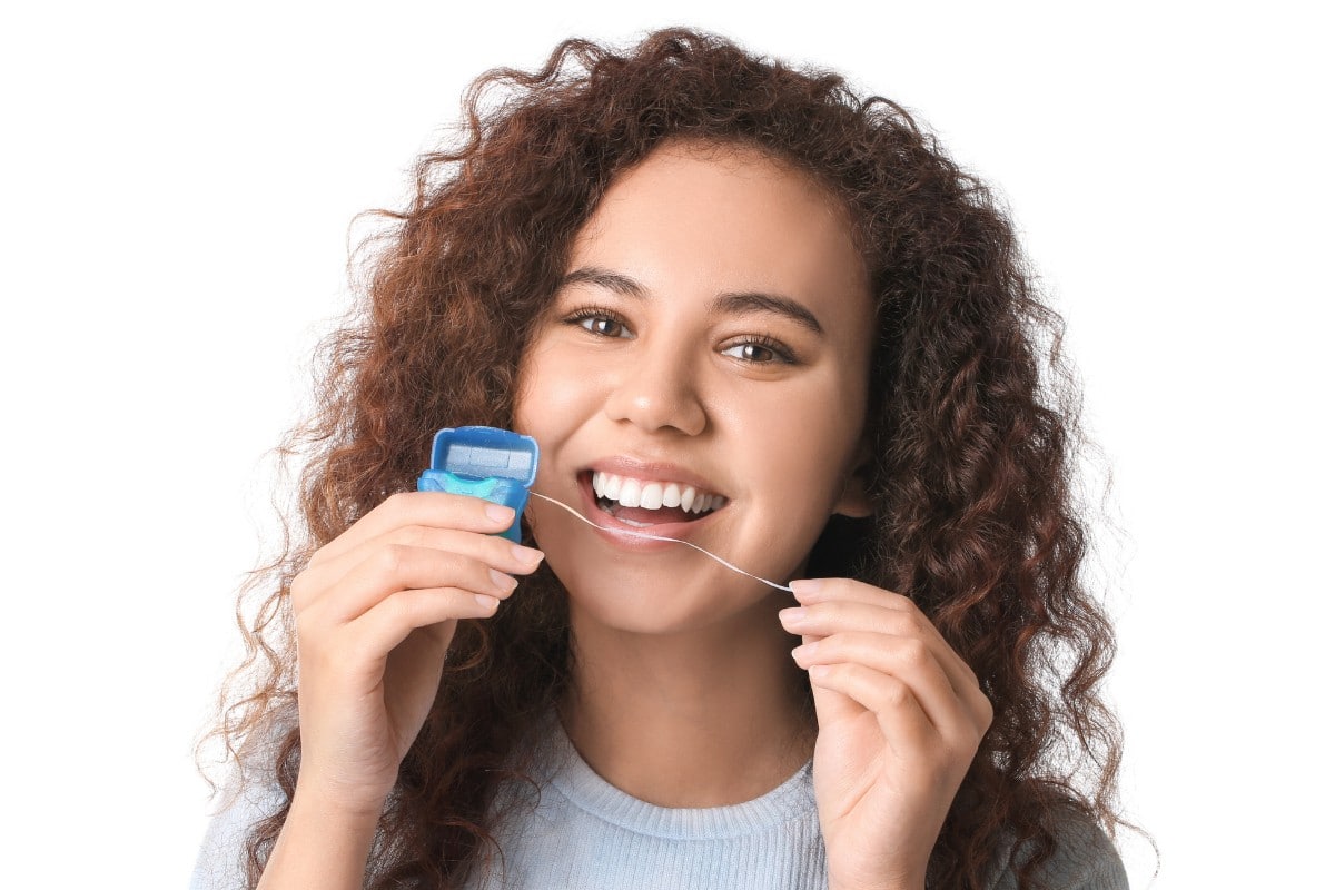What is the Best Kind of Floss to Use Young woman smiling while holding dental floss against white background.